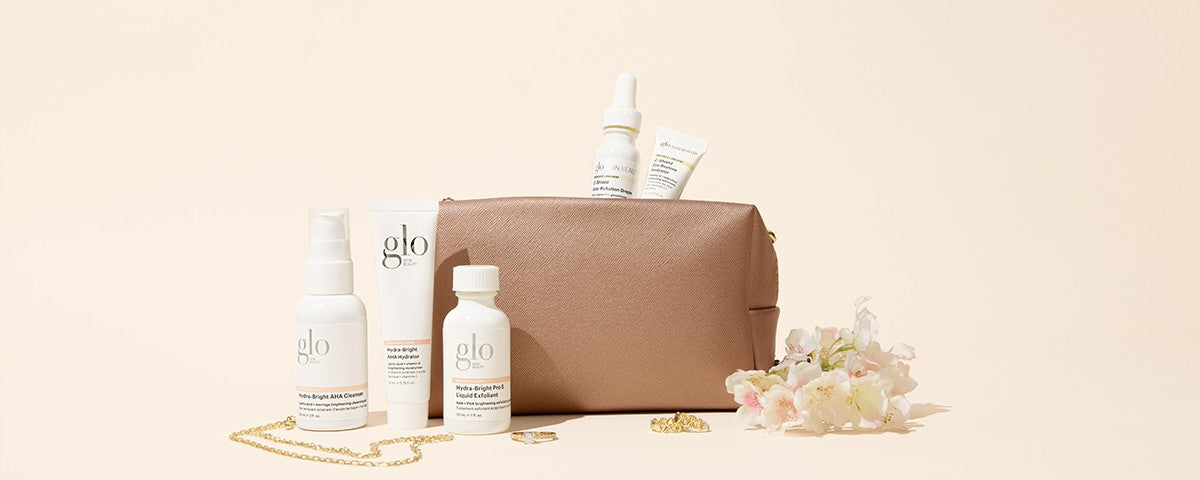 Glo set with brown pouch and flowers, showing labels: Hydra-Bright AHA Cleanser; AHA Hydrator; Pro 5 Liquid Exfoliant