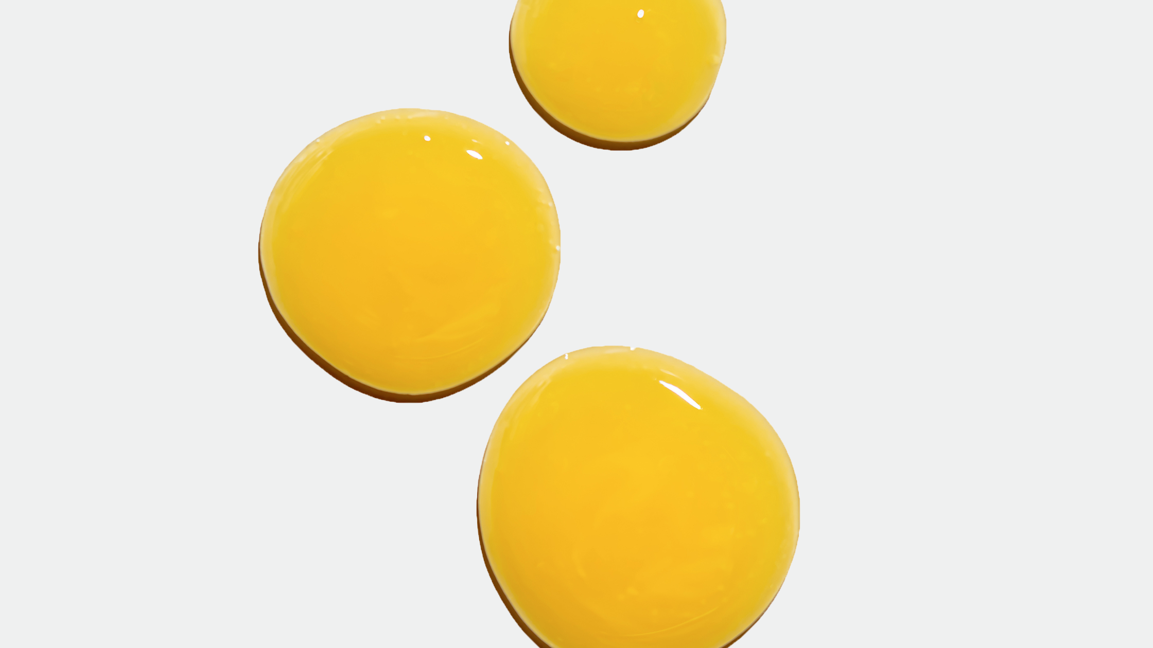 Three glossy yellow serum drops on a pale gray background