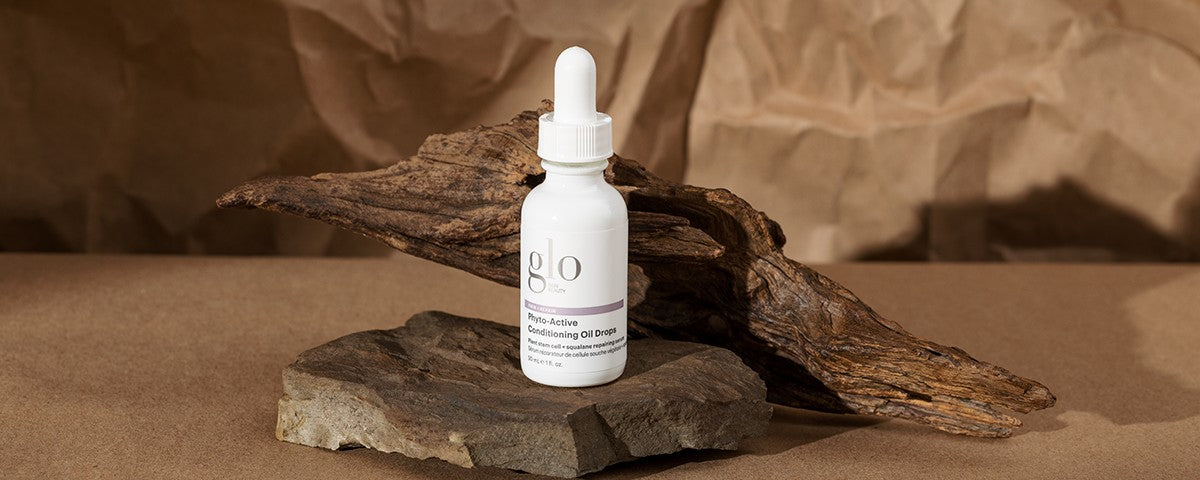glo bottle labeled 'Phyto-Active Conditioning Oil Drops' on driftwood and stone