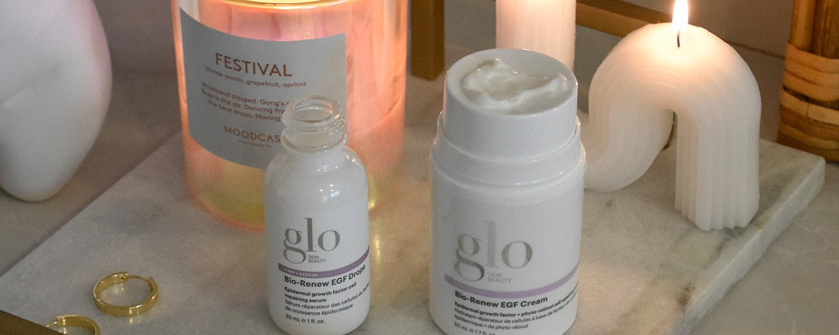 glo Skin Beauty Bio-Renew EGF Drops and Bio-Renew EGF Cream beside FESTIVAL MOODCAST candle on marble with rings