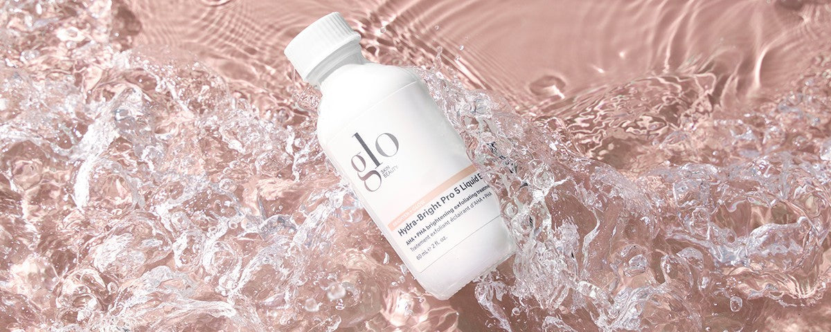White 'glo SKIN BEAUTY' bottle labeled 'Hydra-Bright Pro 5 Liquid Exfoliant 60 mL e 2 fl. oz.' floating in rippling pink water