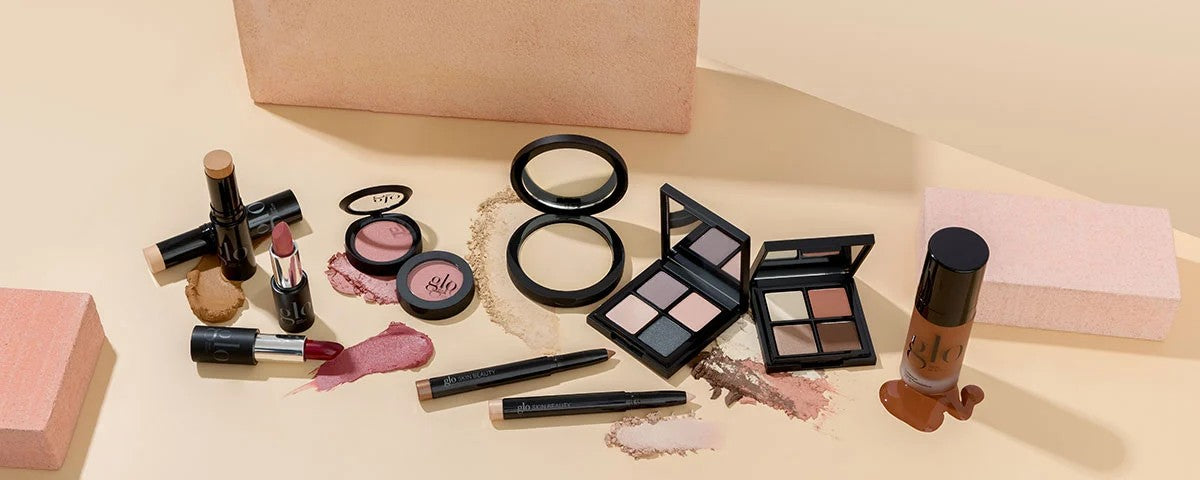glo; glo skin beauty makeup spread — compacts, palettes, lipsticks, pencils, and foundation swatches on beige