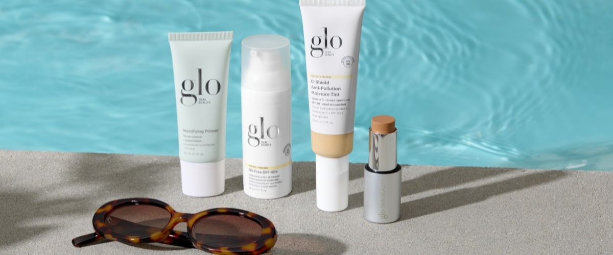Three glo skin beauty products — Mattifying Primer; Oil-Free SPF 40+; C-Shield Anti-Pollution Moisture Tint — plus a foundation stick and sunglasses by a pool.