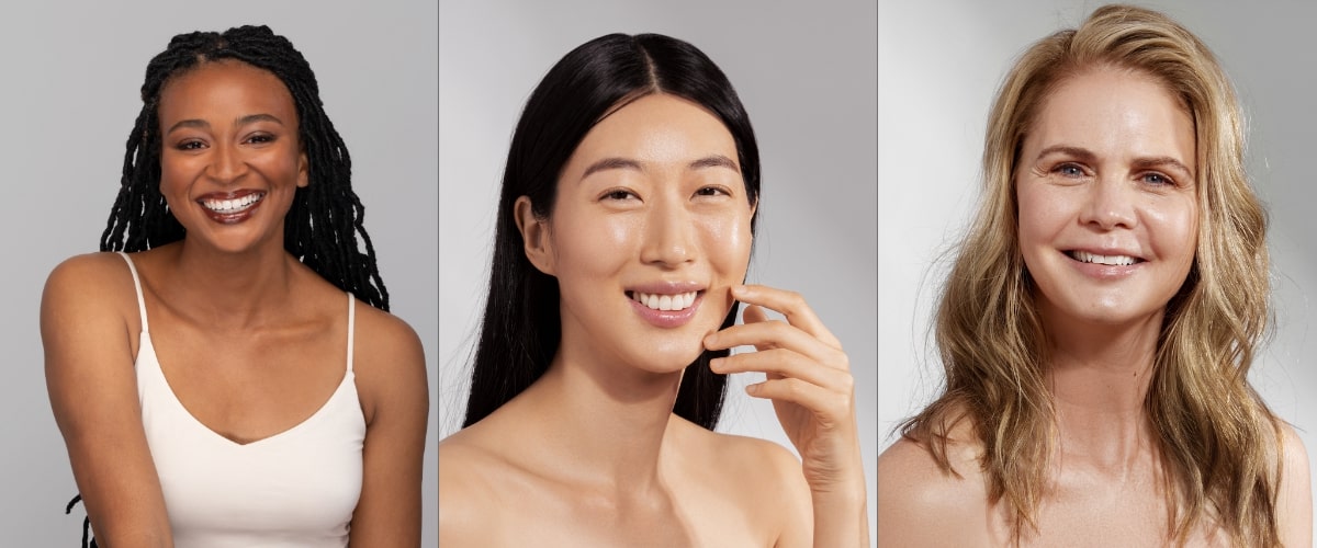 Three smiling women with clear skin — young Black woman with braids, Asian woman touching her face, and smiling middle‑aged white woman
