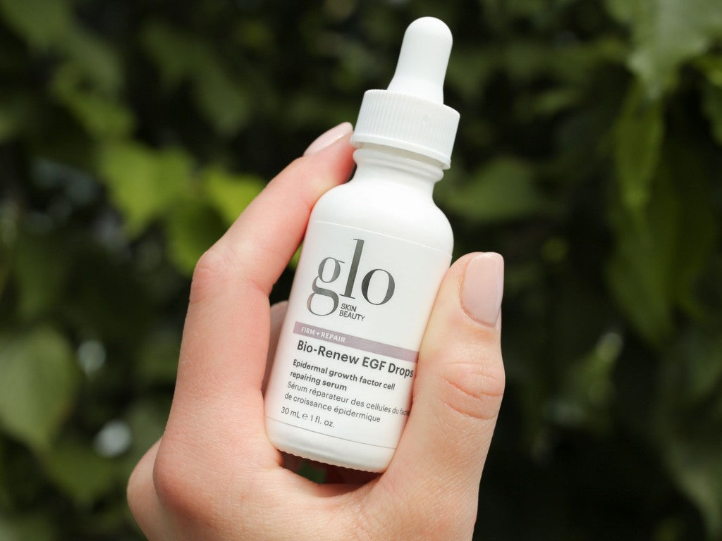 Hand holding white dropper bottle labeled glo SKIN BEAUTY Bio-Renew EGF Drops Epidermal growth factor cell repairing serum