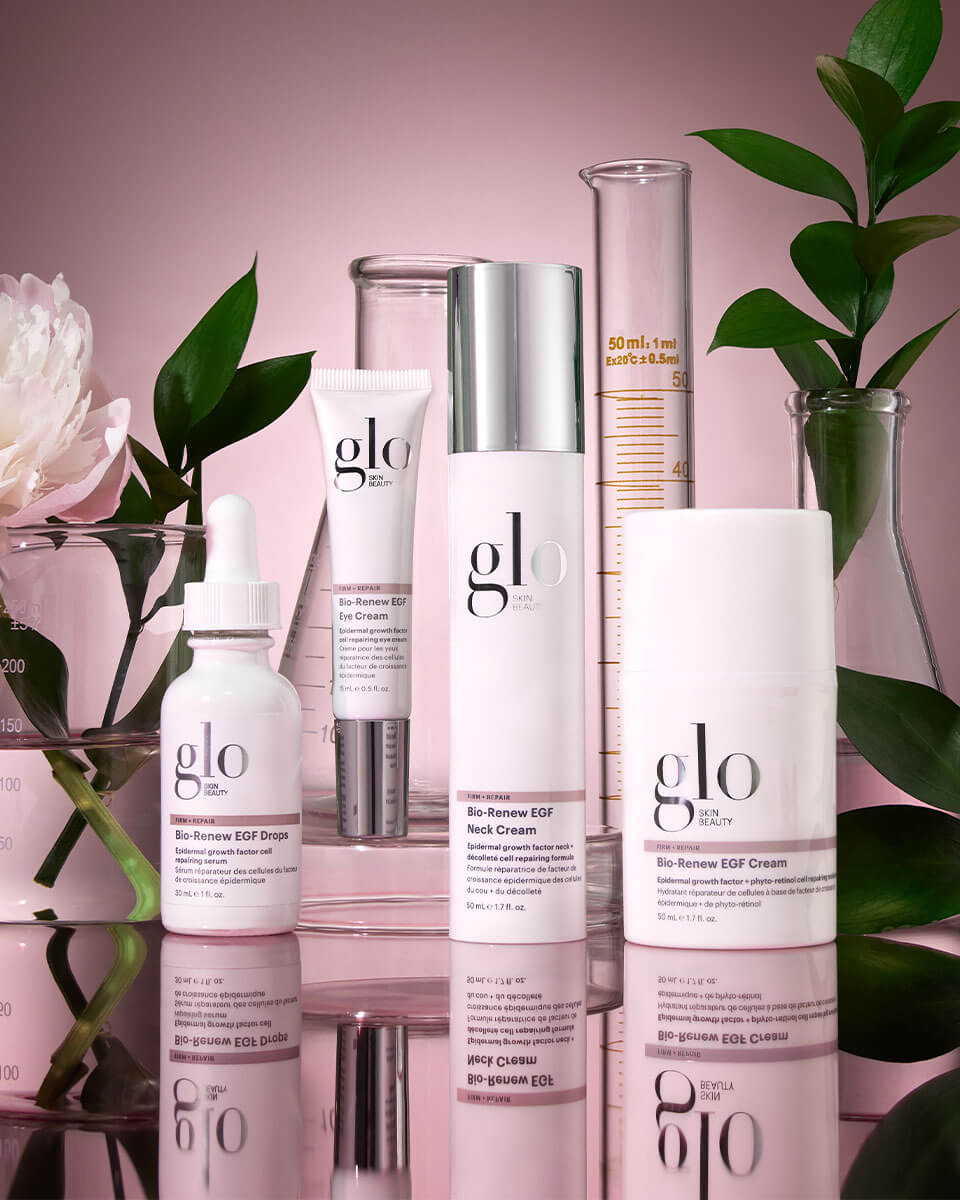 glo Skin Beauty product lineup: Bio-Renew EGF drops, eye, neck, and face creams with glass beakers and leaves on pink background