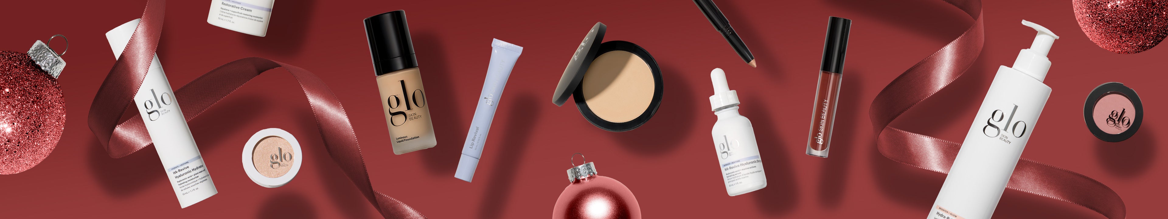Holiday flatlay of glo skin beauty makeup and skincare products with red ribbon and ornaments