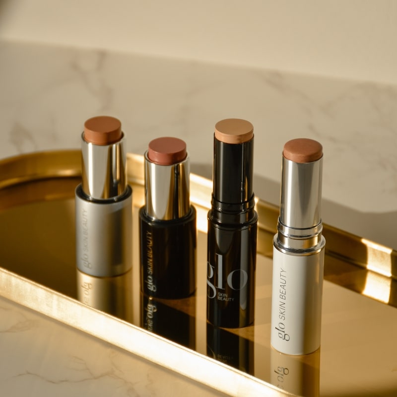 Four contour and highlight cream sticks on a gold tray, labeled glo SKIN BEAUTY.