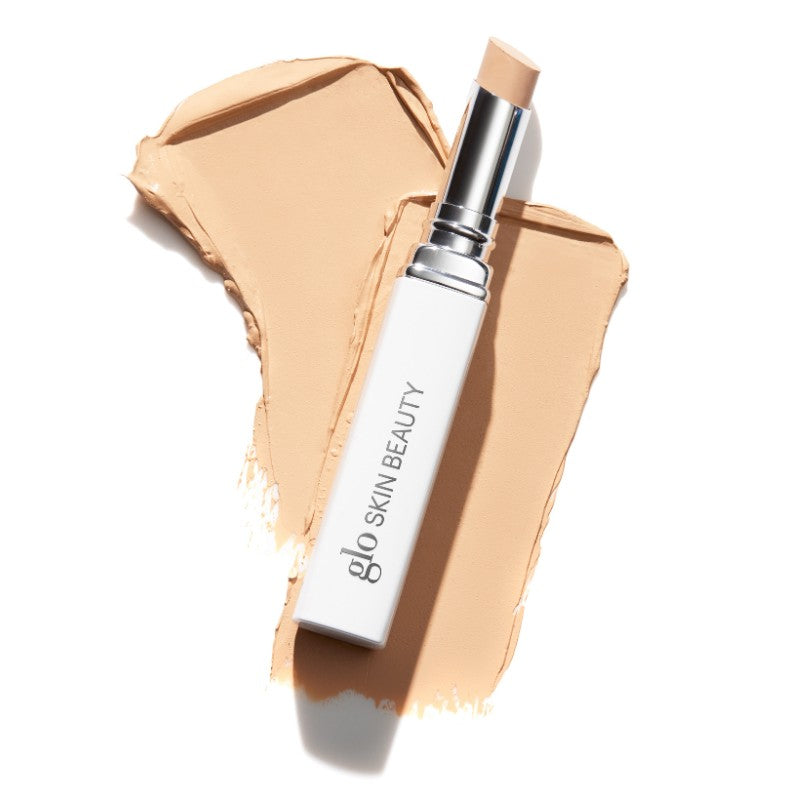 Concealer stick labeled 'glo SKIN BEAUTY' resting on beige makeup swatch