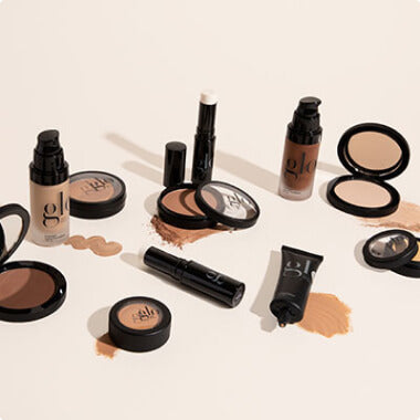 Assorted glo makeup products and compacts arranged with powder smudges on beige background