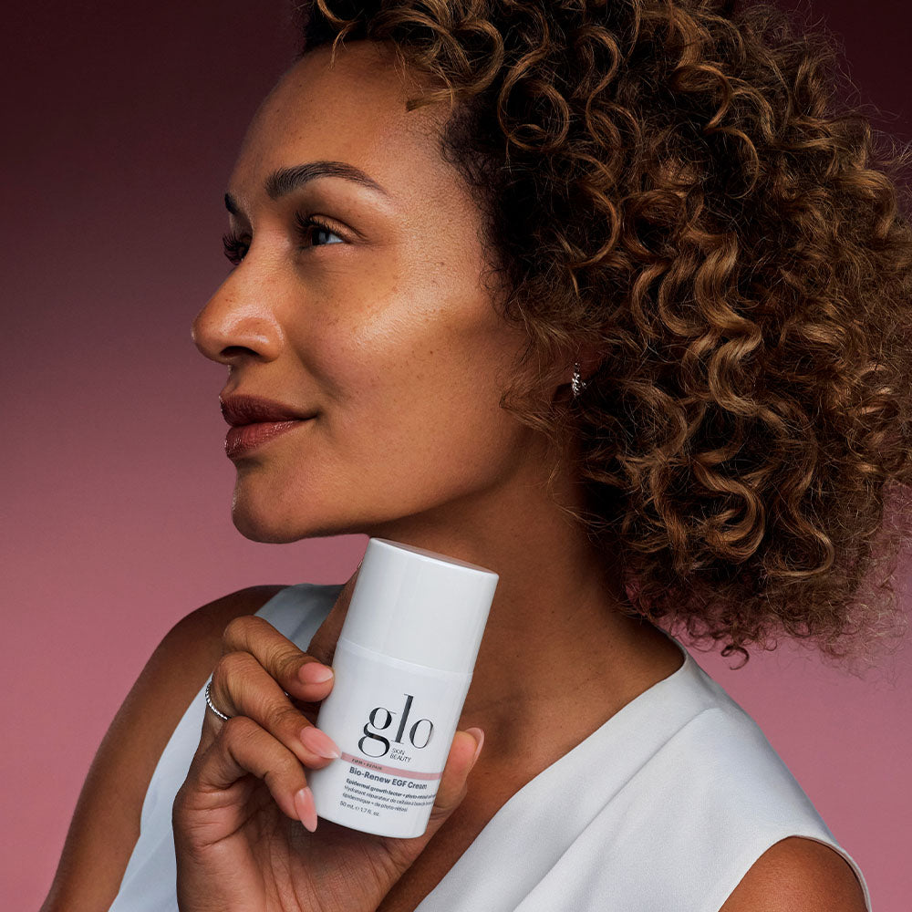 Woman holding Bio-Renew EGF Cream bottle near her chin against a pink gradient background