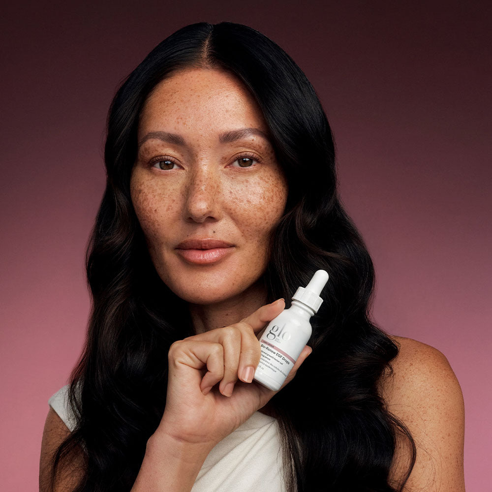 Woman holding a white dropper bottle of Bio-Renew EGF Drops near her face against a pink gradient background