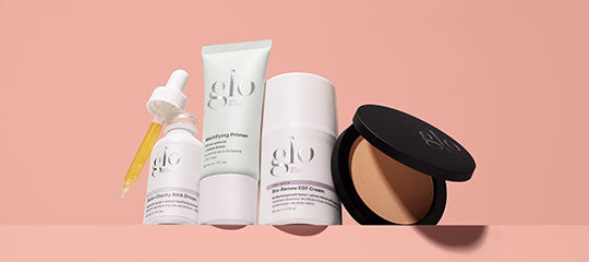 Three glo skincare products — dropper bottle with pipette, primer tube, stick bottle, and open compact on pink background