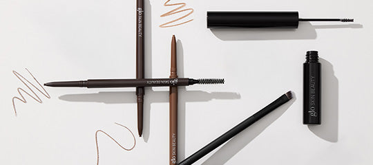 Brown eyebrow pencils, angled brush, mascara tube and swatches on white background; tube labeled glo SKIN BEAUTY
