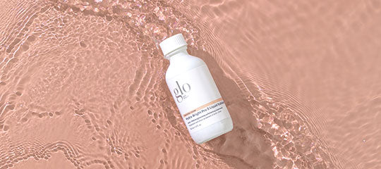 White bottle labeled 'glo' resting on rippled water on pink background
