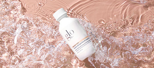 White bottle labeled 'glo' floating in pink water with splashes