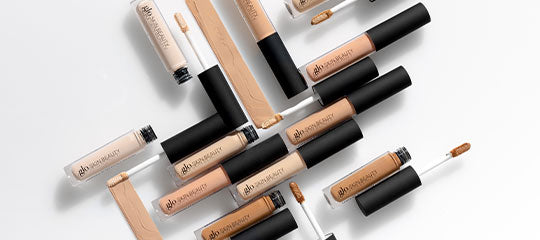 Assorted beige liquid concealer tubes with doe-foot applicators arranged on a white background