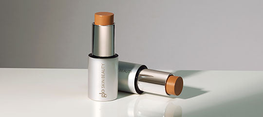 Stick foundation makeup labeled 'glo SKIN BEAUTY' with one stick upright and one lying down