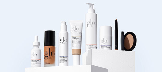 glo skincare and makeup on white pedestals: serums, foundation, tubes, pump bottles, pencil and compact.