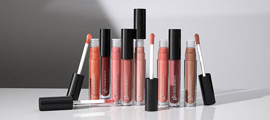 Assorted peach and nude liquid lipsticks with applicators on a reflective surface.