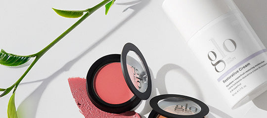 Makeup compacts with a coral swatch beside a bottle labeled 'glo Restorative Cream' on a white background