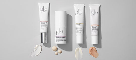 Four glo skincare tubes and pump bottle with cream swatches on a gray background