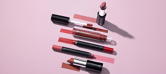 Assorted mauve and pink lipsticks and liquid lip crayons arranged on a pale pink background