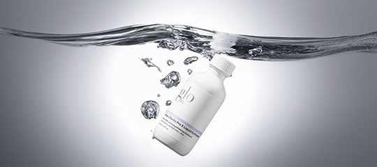 White bottle with 'glo' logo floating just below water surface with bubbles and rippling surface