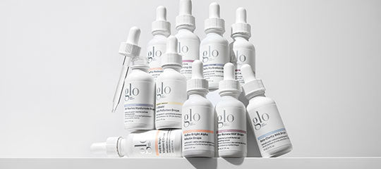 White dropper bottles grouped on a white surface, labeled 'glo'.