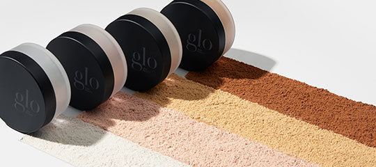Four black 'glo' makeup compacts with five swatches of powder shades from light to dark