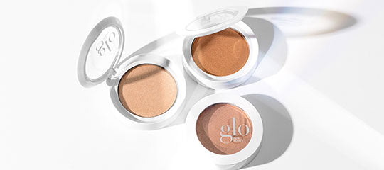 Three white round compacts with beige bronzer shades, one compact showing the word "glo" on its lid.