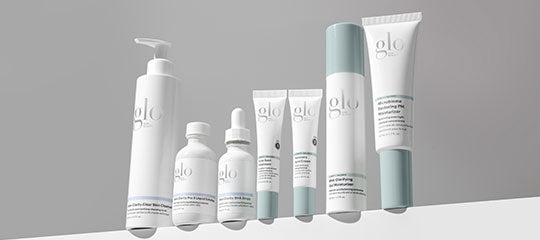glo skincare product line: white and pale teal bottles and tubes arranged on gray background ledge