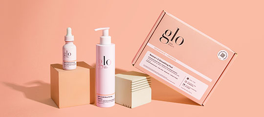 Pink glo skincare set: pump cleanser bottle, dropper serum, and tilted pink glo box on display blocks