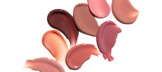 Creamy lipstick swatches in pink, mauve, and nude tones smeared on a white background