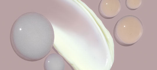 Smear of white cream and several translucent gel droplets on muted mauve background