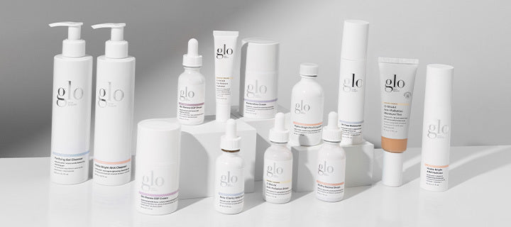 Assortment of white glo skincare bottles, jars, dropper bottles, and a tube displayed on white platforms.