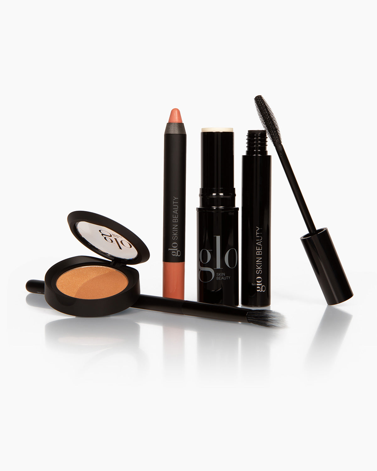 Makeup set: glo SKIN BEAUTY mascara, cream stick, lip crayon, compact powder and brush on white background