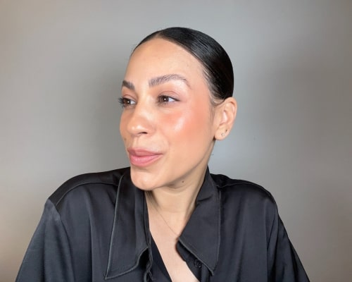 Woman wearing a black blouse showing cream blush on her cheeks, looking slightly left