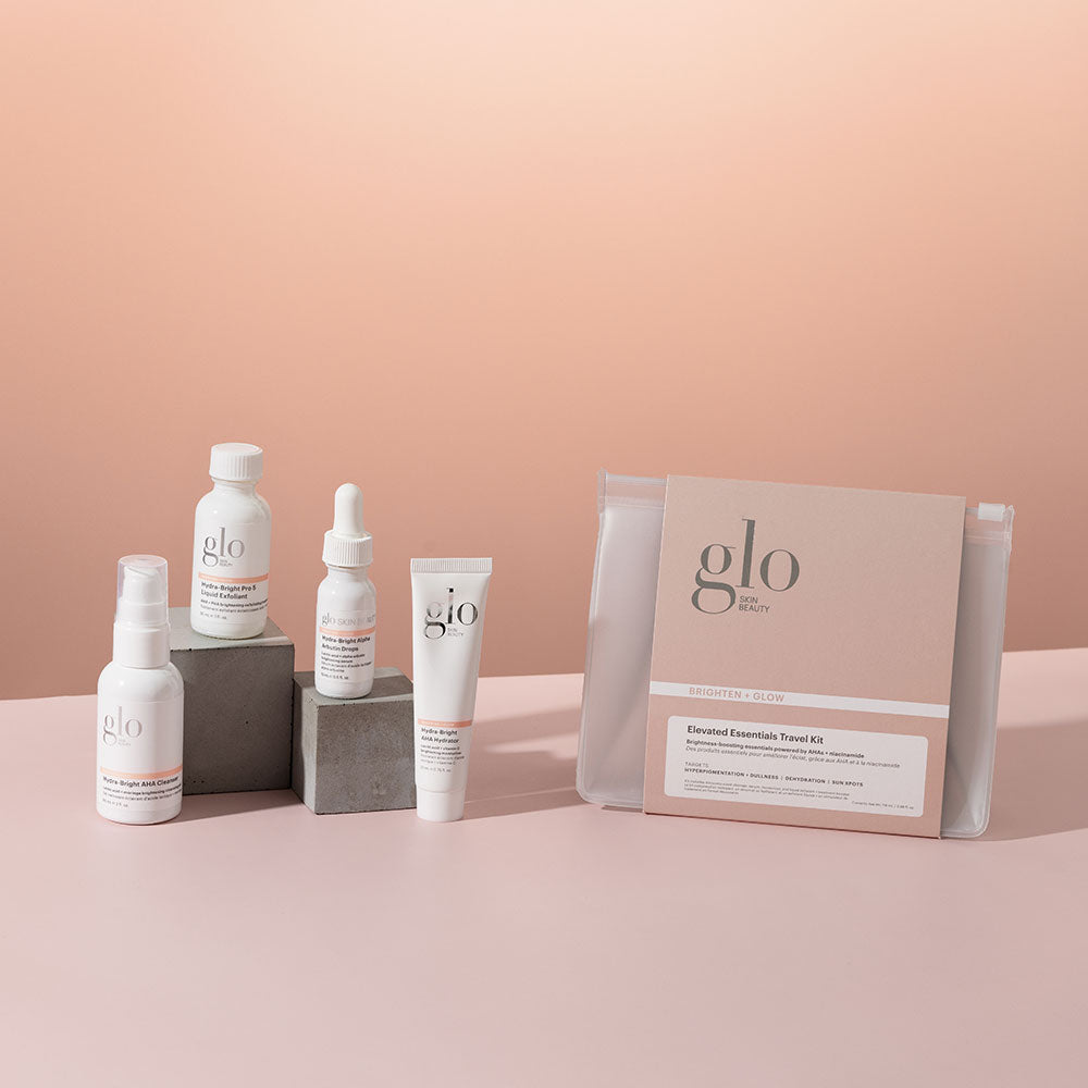 Skincare products including bottles, dropper, tube, and Elevated Essentials Travel Kit pouch labeled 'glo'.