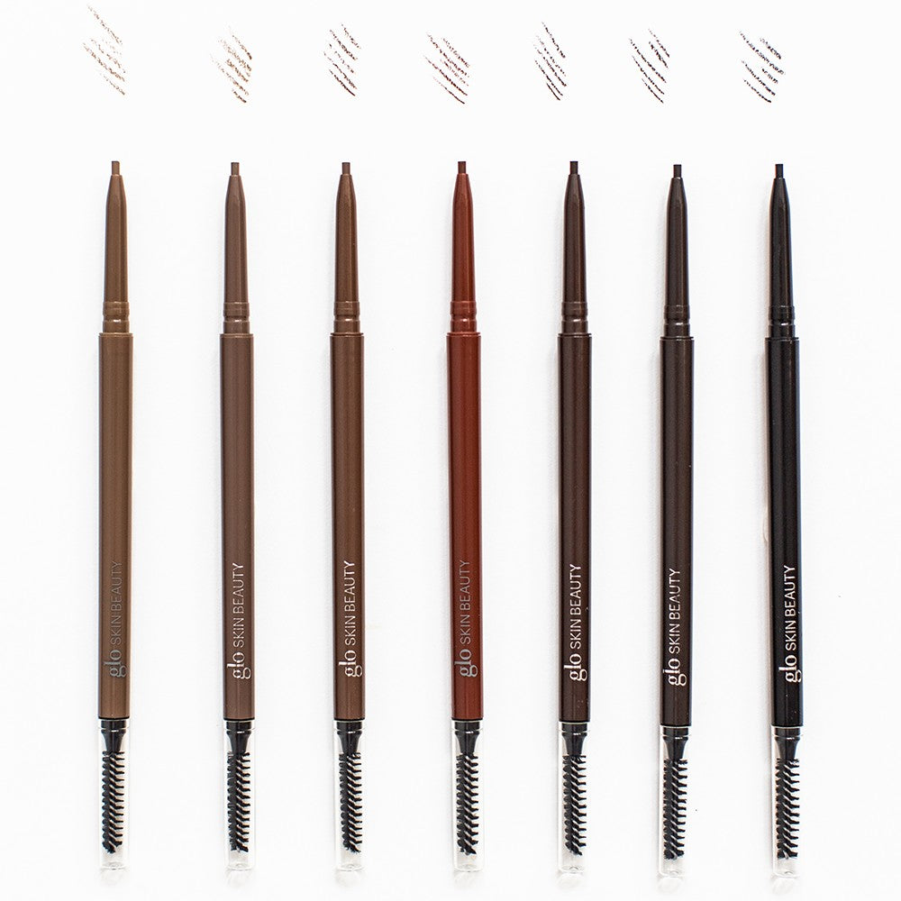 Seven glo SKIN BEAUTY eyebrow pencils in varying brown to black shades with spoolie brushes on one end.