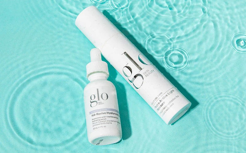 White glo bottles on aqua water; dropper labeled 'HA-Revive Hyaluronic' and tube labeled 'glo Hydra-Active Light Moisture'