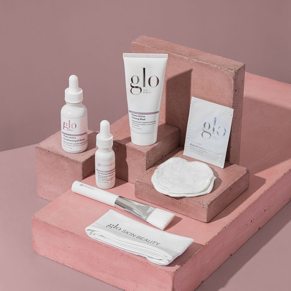 Assorted glo SKIN BEAUTY products on pink blocks: Phyto-Active Conditioning Oil Drops, Phyto-Active Firming Mask, Phyto-Active Cream Cleanser, Bio-Renew EGF, brush and cloth