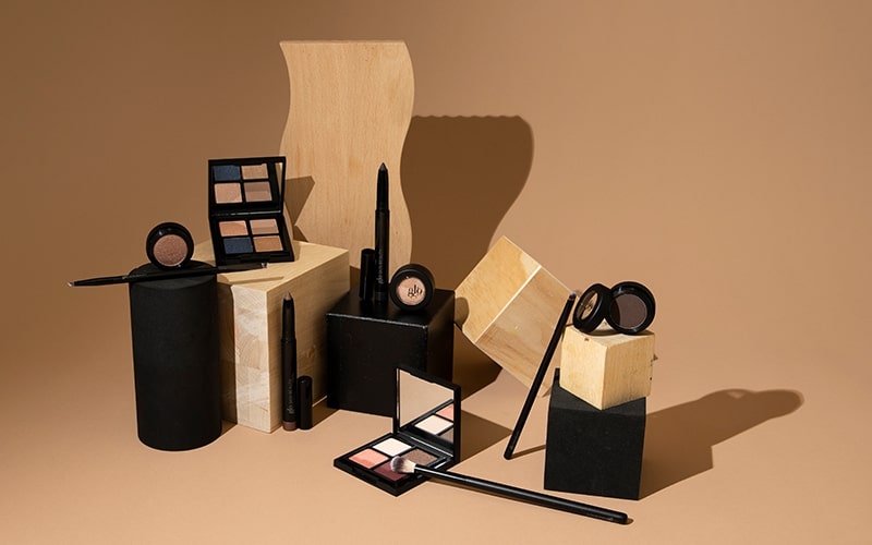 Neutral eyeshadow palettes, compacts and makeup brushes arranged on a beige background