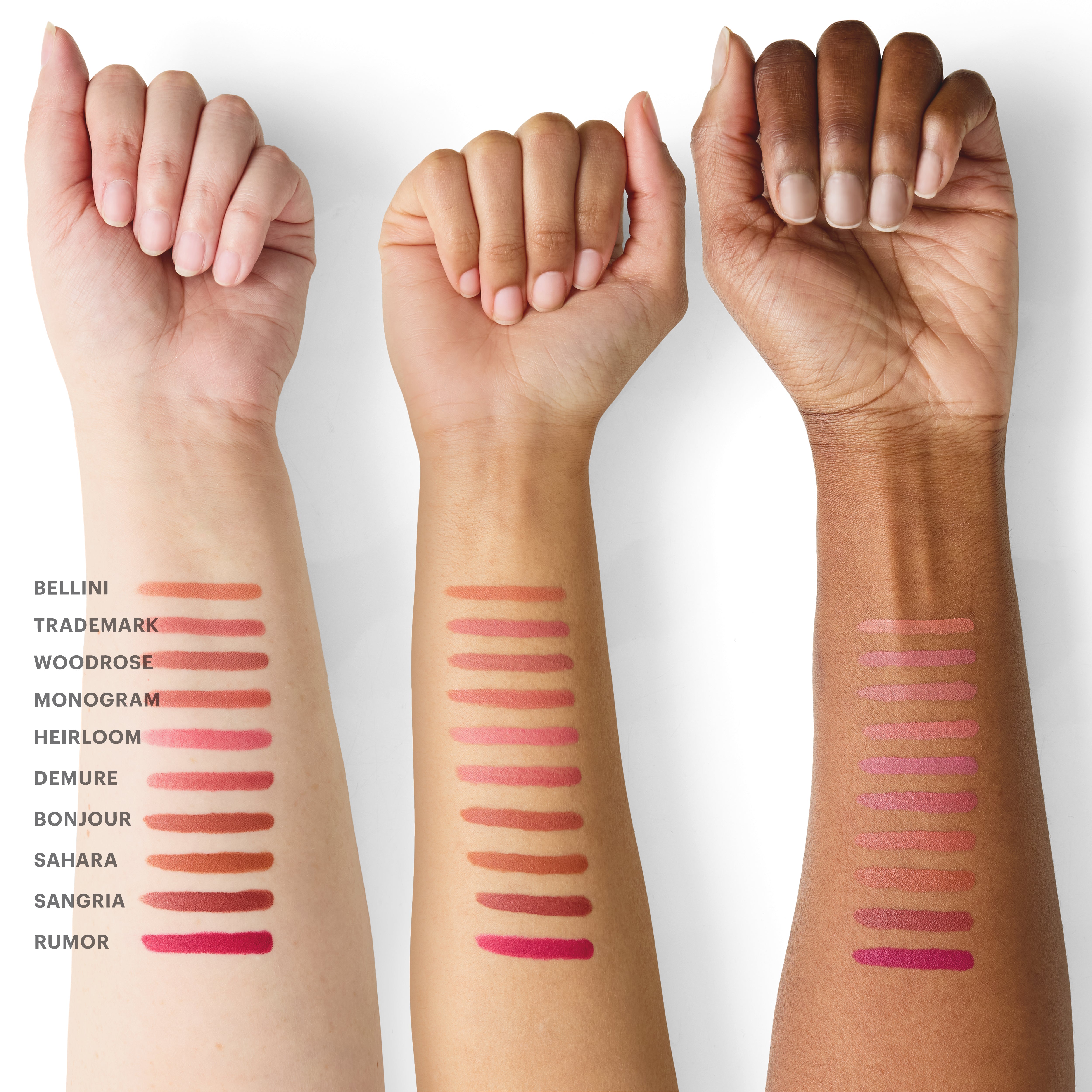 Three forearms with lipstick swatches labeled BELLINI TRADEMARK WOODROSE MONOGRAM HEIRLOOM DEMURE BONJOUR SAHARA SANGRIA RUMOR