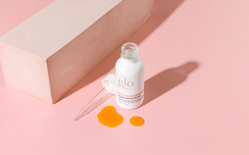 glo bottle labeled 'GlyPro Retinol Drops' with dropper and two orange drops on pink background