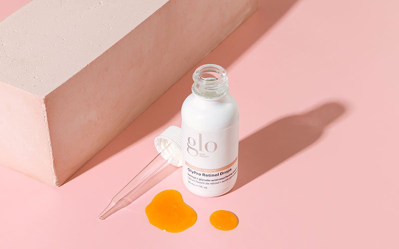 glo bottle labeled 'GlyPro Retinol Drops' with pipette and two orange drops on pink background