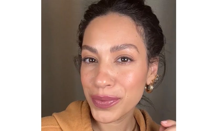 Close-up portrait of a smiling woman with glossy mauve lipstick and gold hoop earrings