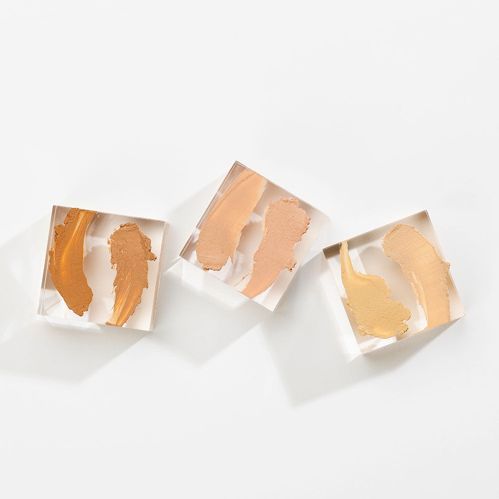 Three concealer swatches in varying beige and tan shades on clear square blocks