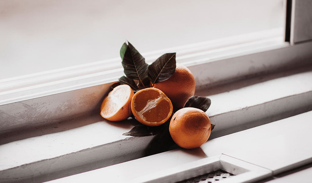 Oranges and green leaves on a white windowsill, one orange halved to show its segments.
