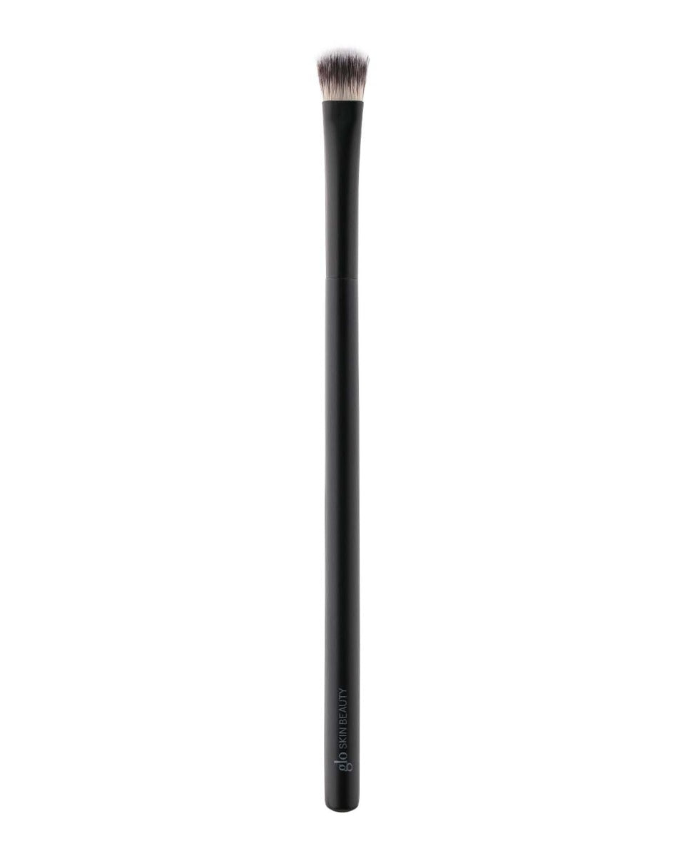 Black-handled small rounded-top makeup brush with dense synthetic bristles; handle reads 'glo SKIN BEAUTY'.